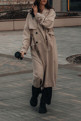 Street style photography with fashionable details of a beige long seasonal trench coat, a woman...