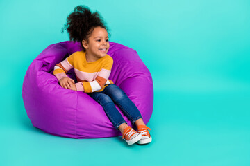 Photo of nice curious cute small lady sit beanbag look empty space wear striped pullover isolated...
