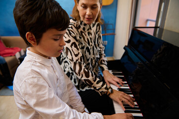 Teenager boy having music lesson at home, sitting near his pianist teacher, playing piano forte