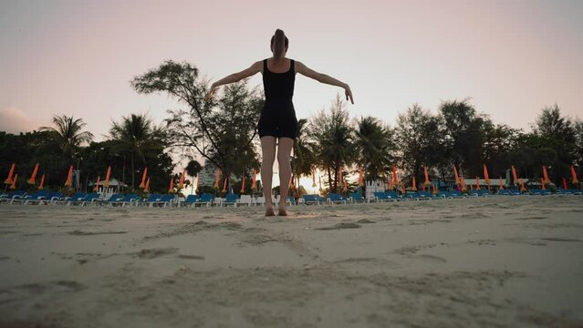 Barefooted woman doing yoga exercise lounge, warrior pose on sandy sea ocean beach at sunset. Female stretching legs. Body care, wellness, sportswear, sport training morning sporty outdoors concept.