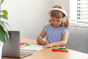  Online education. A girl with headphones listens to a teacher using a laptop at home. Education