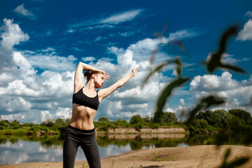 athletic young woman in the summer outdoors on the river bank in nature doing fitness and sports