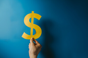 Hand Holding Golden Dollar Sign Against Blue Background Symbolizing Financial Success and Economy