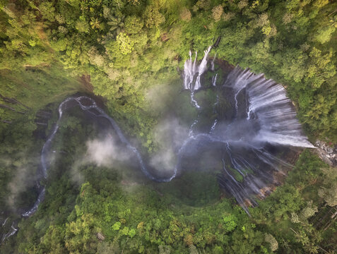 Top view of a sprawling waterfall cascading into a serene pool, nestled within the dense greenery of a tropical forest