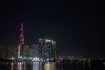 The Saigon river with the skyline of Ho Chi Minh City (Saigon), Vietnam, and the purple illuminated tower Landmark 81 in the background at night