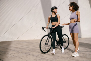 Two sporty female friends talking while standing in city before training