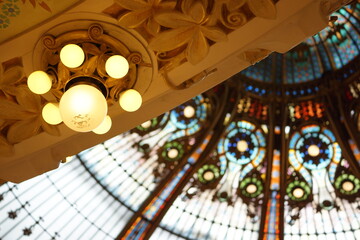 Light fixture in foreground, interior of beautiful stained glass dome in background