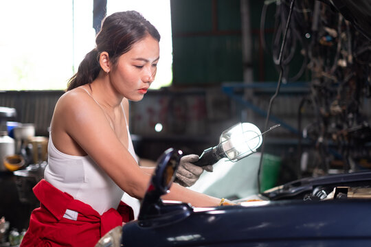 Female Mechanic Working Under Vehicle in a Car Service. Empowering Woman Wearing Gloves and Using a Ratchet Underneath the Car. Modern Clean Workshop.
