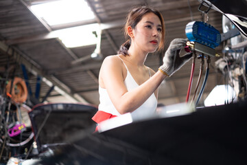 Female Mechanic Working Under Vehicle in a Car Service. Empowering Woman Wearing Gloves and Using a...