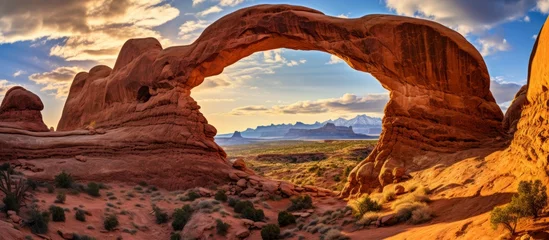 Fotobehang The large arch stands prominently in the desert landscape, framed by the vast blue sky in the background © AkuAku