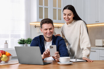 Happy couple using smartphone together at wooden table in kitchen