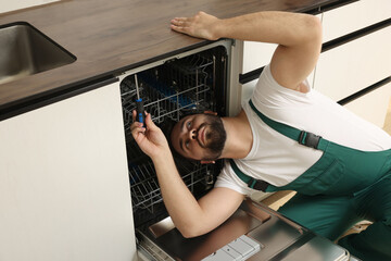 Serviceman repairing dishwasher with screwdriver in kitchen