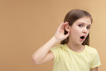 Little girl with hearing problem on pale brown background, space for text