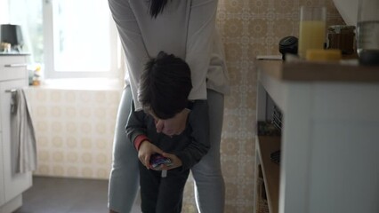 Mother and child standing at kitchen in authentic genuine everyday moment. Candid real life family scene of mom and 5 year old son hanging at home