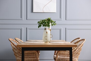 Rattan chairs, table, burning candles and vase with green branches in stylish dining room