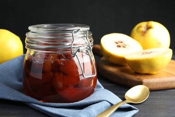 Quince jam in glass jar, spoon and fresh raw fruits on grey table, closeup