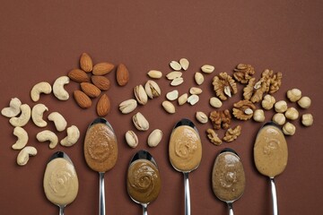 Tasty nut butters in spoons and raw nuts on brown table, flat lay