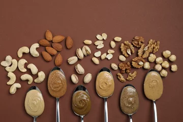 Poster Tasty nut butters in spoons and raw nuts on brown table, flat lay © New Africa