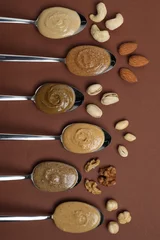 Poster Tasty nut butters in spoons and raw nuts on brown table, flat lay © New Africa