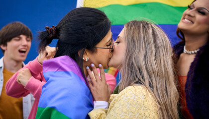 Young Caucasian lesbian couple kissing lovingly with rainbow flags celebrating with LGBT community...