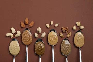 Foto op Canvas Tasty nut butters in spoons and raw nuts on brown table, flat lay. Space for text © New Africa