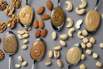 Poster Tasty nut butters in spoons and raw nuts on gray table, flat lay © New Africa