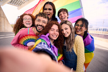 Group of young diverse friends taking a selfie looking at front camera of mobile celebrating gay...