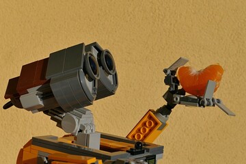 Fototapeta premium LEGO robot Wall-E from Disney Pixar animated movie of the same name, holding slice of tangerine in his left arm, yellow wall in background. 