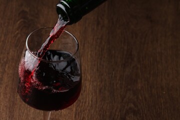 Pouring tasty red wine in glass at wooden table, closeup. Space for text
