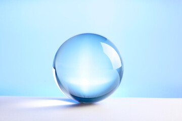 Fototapeta na wymiar Transparent glass ball on table against light blue background