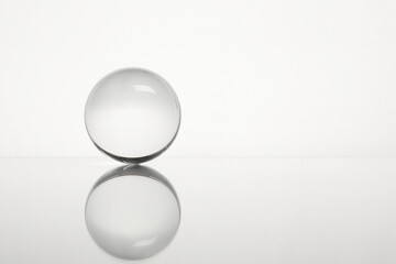 Transparent glass ball on mirror surface against white background. Space for text