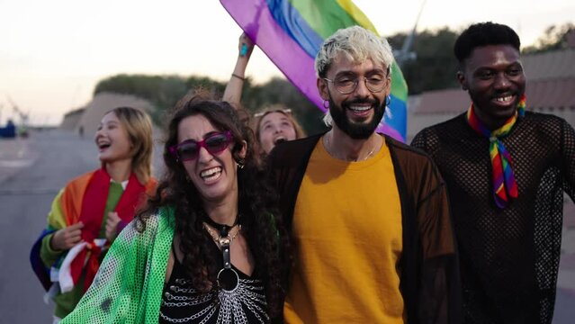 A group of LGBT people is leisurely walking down the street in the gay pride day parade holding colorful rainbow flags, enjoying a fun, friendship and happy event. Diverse men and women run together
