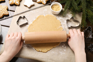 Making Christmas cookies. Woman rolling raw dough at wooden table, top view