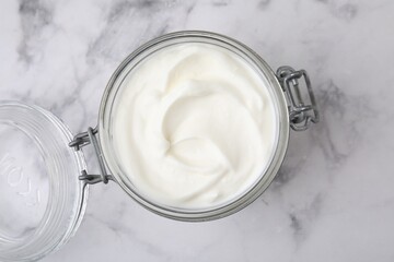 Delicious natural yogurt in glass jar on white marble table, top view