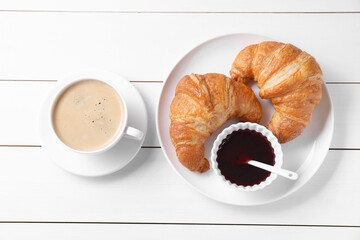 Fresh croissants, jam and coffee on white wooden table, flat lay. Tasty breakfast