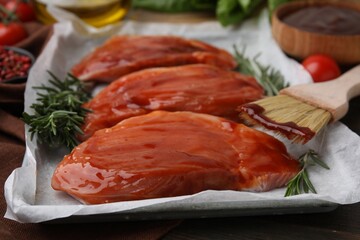 Raw marinated meat, rosemary and basting brush on table, closeup