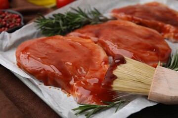 Raw marinated meat, rosemary and basting brush on table, closeup