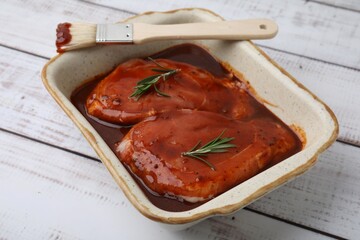 Raw marinated meat, rosemary and basting brush on white wooden table, closeup