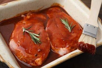 Raw marinated meat, rosemary and basting brush on table, closeup