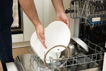 Man loading dishwasher with plates indoors, closeup