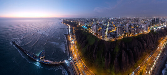 Panoramic aerial view captured with a drone, of the Miraflores district, in Lima, Peru.  The cliffs, the "Costa Verde" highway, the Miraflores boardwalk and the Pacific Ocean with the sky at sunset.