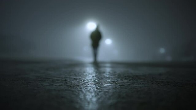 The silhouette of man walking on empty parking lot at fogy night time