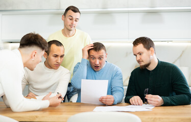 Fototapeta premium Brainstorming - male friends trying to solve financial problems by consulting at the table in the home kitchen