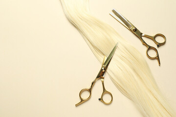 Professional scissors with blonde hair strand on beige background, flat lay. Space for text