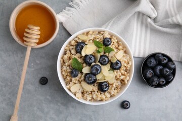Tasty oatmeal with blueberries, mint and almond petals in bowl on grey table, flat lay