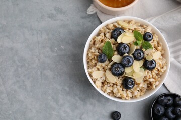 Tasty oatmeal with blueberries, mint and almond petals in bowl on grey table, flat lay. Space for text