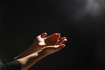 Religion. Woman with open palms praying on black background, closeup. Space for text