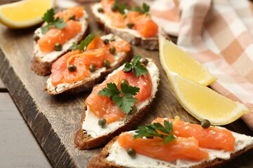 Tasty canapes with salmon, capers, lemon and cream cheese on wooden table, closeup