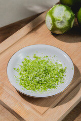 close up of lime grated zest on saucer over cutting board  and a grated lime behind