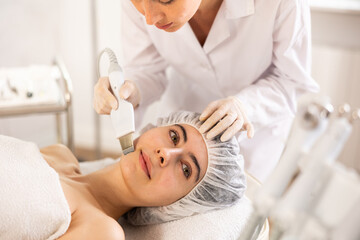 Young woman cosmetologist performs hardware facial exfoliating procedure to young female patient